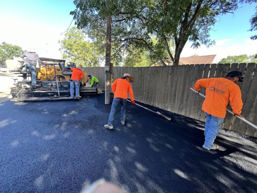 Crew raking and leveling fresh asphalt along a fence