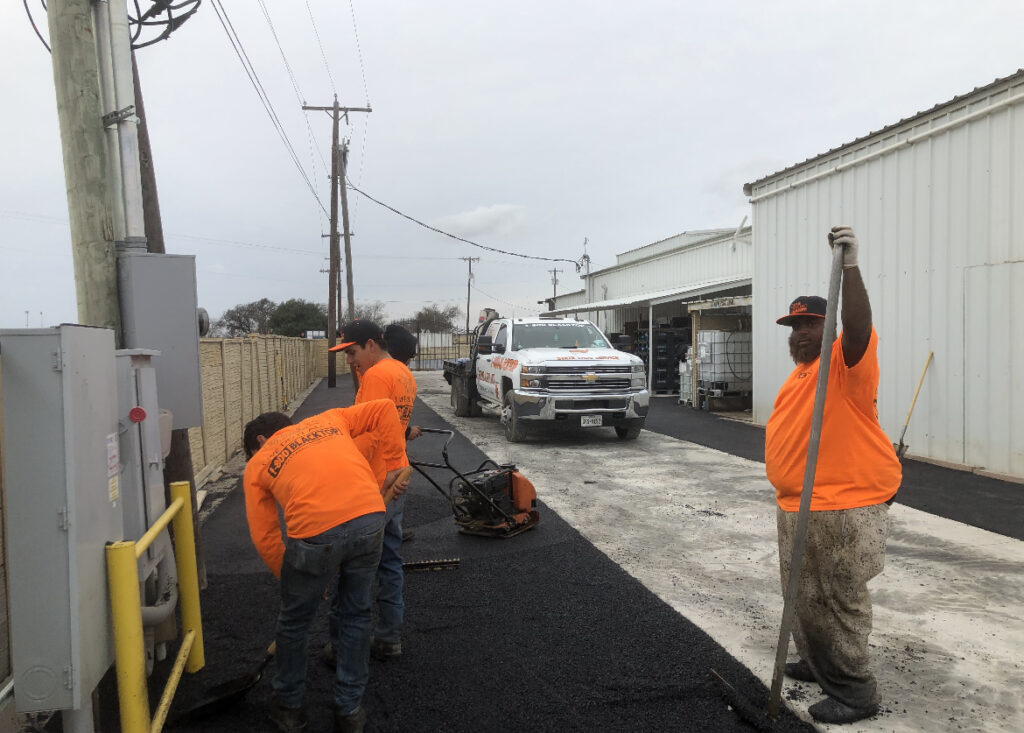 Crew patching asphalt behind a building