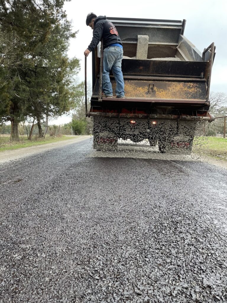 Spreading chip seal stone from a dump truck on a gravel drive